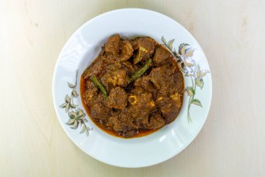 Ahşap zemin üzerinde beyaz seramik tabakta lezzetli körili koyun eti. Koyun bhuna popüler, lezzetli ve baharatlı bir Bangladeş yemeğidir. Üst görünüm.