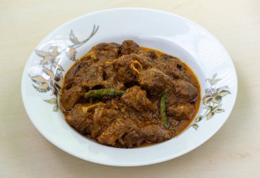 Ahşap bir arka planda beyaz tabakta lezzetli körili koyun eti. Koyun bhuna popüler, lezzetli ve baharatlı geleneksel bir Bangladeş yemeğidir..