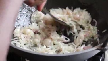 Tavada yağda kızartılan soğan, spatulayla karıştırılan kadın eli. Peyaj beresta yapmak için ince dilimlenmiş soğanın yakın plan görüntüsü..
