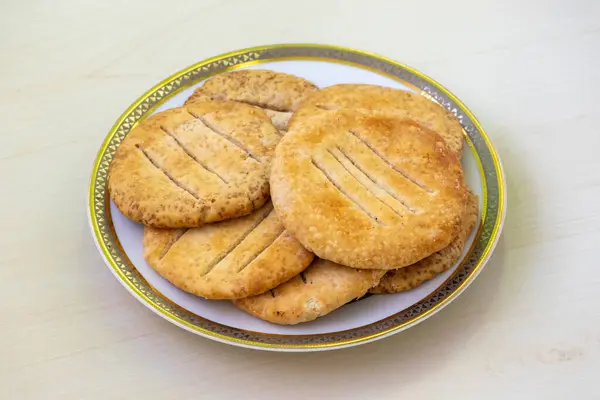 stock image Delicious crispy Bakarkhani on a white plate on wooden background. Baqarkhani is a thick spiced flatbread that originated in Bangladesh during the Mughal period.