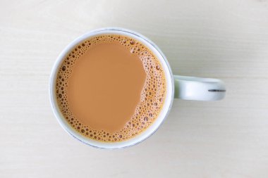 Bir fincan sütlü çay ya da açık ahşap yüzeyde seramik bir fincanda dudh cha. Üst görünüm.