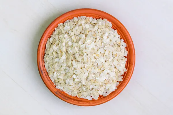 stock image Raw flattened rice or chira on a clay plate on a light wooden surface. It is also known as poha, pohe, aval, pauwa, sira, chivda, or avalakki. Top view.