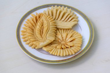 Tahta bir yüzeyde beyaz bir tabakta çıtır çıtır Nakshi Pitha. Geleneksel bir Bengali (Bangladeş) yiyeceğidir ve Pakkon Pitha olarak da bilinir. Bu pitha türü pirinç unundan yapılır..