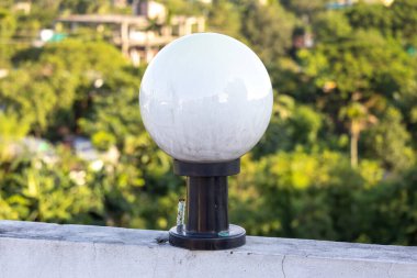 Beyaz yuvarlak cam lamba. Siyah çelik bir direğe monte edilmiş. Evin duvarına monte edilmiş..