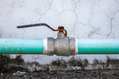 Evin çatısındaki su tesisat borusunun ve vananın yakın planında eski bir beton duvar arka planına kurulmuş bir su sistemi var..