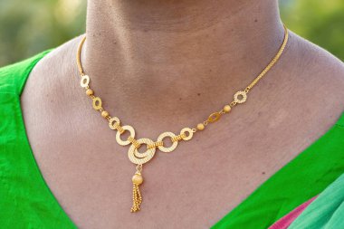 Madalyonla süslenmiş güzel bir Asyalı kadının boynuna yakın çekim. Kolyeli modern lüks altın kolye. Güzellik ve moda aksesuarları.