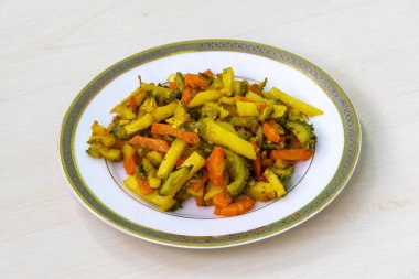 Pişmiş patates, havuç ve beyaz tabakta acı kabak böreği. Sebzeler doğranıyor, karıştırılıyor ve kızartılıyor. Bu popüler Bangladeş yemeği sebze karışımı nedeniyle sağlıklıdır..