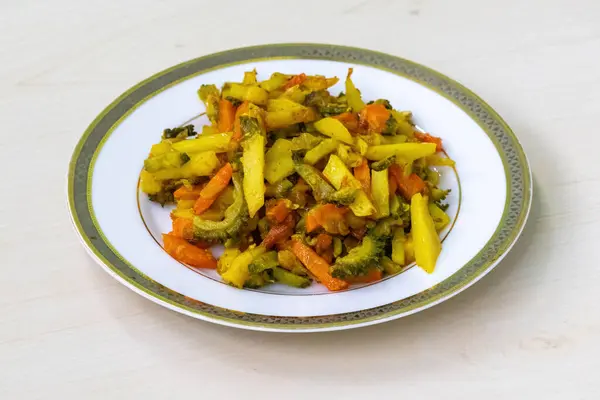 stock image Cooked potato, carrot, and bitter gourd fritters on a white plate. These vegetables are chopped, mixed together, then fried. This Bangladeshi dish is a healthy option due to its mix of vegetables.