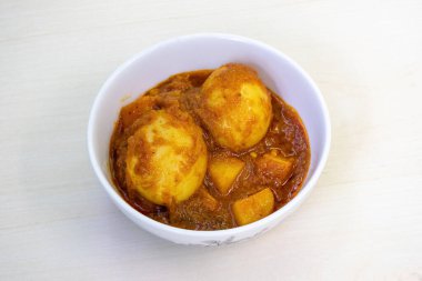 Spicy egg curry or Dim Vuna, cooked with potato, in a white ceramic bowl, placed on a light wooden surface. Boiled dim bhuna is a flavorful bengali recipe that is often enjoyed with rice or bread. clipart