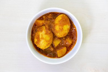 Beyaz bir seramik kasede patatesle pişirilmiş baharatlı yumurta körisi ya da Dim Vuna, açık ahşap bir yüzeye yerleştirilmiş. Lezzetli kaynamış Dim Bhuna 'nın üst görüntüsü, Bengali tarifi çoğunlukla pirinç veya ekmekle yapılır..