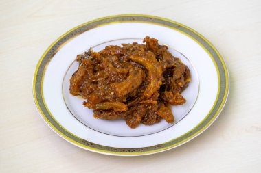 Beyaz bir tabakta servis edilen ev yapımı fil elması turşusu (chalta achar). Bu Dillenia indica turşusu lezzetli bir ekşi, baharatlı ve tatlı lezzet karışımı sunar..