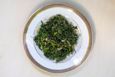 Hafif ahşap bir yüzey üzerinde beyaz bir tabakta servis edilen kızartılmış jüt yaprakları Bangladeş 'te Pat the Bangladeş olarak bilinen besleyici yeşil yapraklı bir sebzedir. Sağlıklı beslenme konsepti. Üst görünüm.