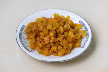 Bir tabak kuru üzüm, açık ahşap bir yüzeyde duruyor. Kuru üzümler çiğ yenebilir ya da pişirme, pişirme ve demleme için kullanılabilir..