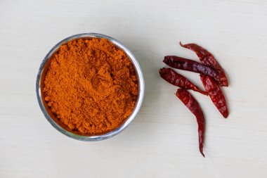 Çelik bir kapta kırmızı biber tozu, yanında da kurutulmuş kırmızı biber var. Üst görünüm.