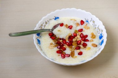 Delicious homemade payesh or payasam, served in a white bowl with a spoon on a wooden background. Made with milk, sugar, and rice, it's garnished with cashew nuts, raisins, pomegranate, and peanuts. clipart