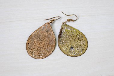Hafif ahşap bir yüzey üzerinde sergilenen, lüks çiçek desenleri ve metal kanca tokaları olan bir çift antika küpe..