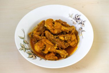 Beyaz bir tabakta servis edilen ev yapımı, lezzetli bhuna balıklı tavuk, ahşap bir yüzeyde dinleniyor. Lezzetli bir Bengalce (Bangladeş yemeği).