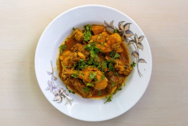 Ev yapımı, nefis körili tavuk kişniş yapraklarıyla süslenmiş, beyaz tabakta servis ediliyor. Lezzetli bir Bengali yemeğinin üst görüntüsü.