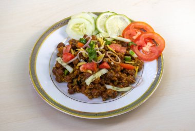 Lezzetli bir tabak chola chana bhuna veya baharatlı nohut, yanında ferahlatıcı domates, limon ve salatalık salatası. Beyaz bir tabakta, ahşap bir arka planda sunuldu..