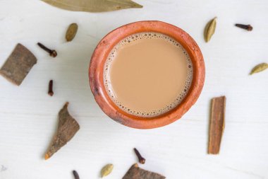 Top view of a cup of hot masala tea, or Indian Kadak Chai, served in a clay cup on a wooden surface. clipart