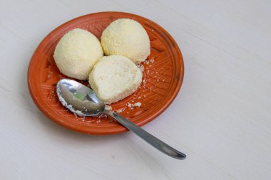 Lezzetli Kachagolla tatlıları ve bir kaşık, kil tabakta servis edilir, hafif ahşap bir yüzey üzerinde dinlenir. Yumuşak, süngerimsi dokusu ve ince tatlılığıyla tanınan popüler bir Bengali tatlısıdır..