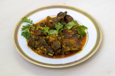 Beyaz bir tabakta servis edilen, kişniş yapraklarıyla süslenmiş lezzetli balık bhuna körisi..