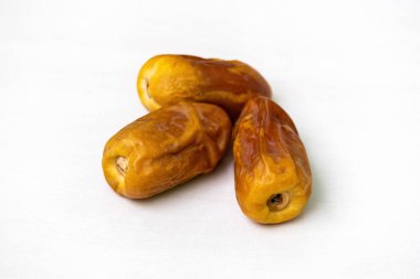 Beyaz bir zemin üzerinde üç kuru hurma meyvesi..