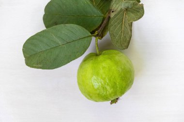 Taze, olgun bir guava meyvesi, sapı ve yeşil yaprakları ile birlikte beyaz arka planda izole edilir. Üst görünüm.