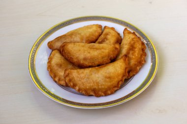 Lezzetli Tavuk Puli Pitha, kızartılmış ve ahşap bir zeminde beyaz bir tabakta servis edilmiş. Bangladeş 'teki bu popüler geleneksel pasta sebze, balık, et, hindistan cevizi ve jaggery dolgularından yapılır.