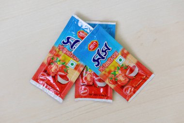 PRAN Sıcak Domates Sosu Mini paketleri hafif ahşap bir yüzey üzerinde duruyor. Ateşli lezzetlerle dolu bu keskin sos, yemek pişirmek ve atıştırmalıklarla eğlenmek için idealdir. Üst görünüm.