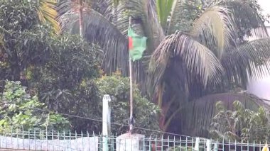Bangladeş 'in ulusal bayrağı, belirgin yeşil ve kırmızı renkleri ile, binanın tepesinde ulusun doğal çevreye karşı bir sembolü olan meltemde dalgalanıyordu..