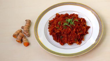 Çiğ zerdeçal kızartması ya da kacha holud bhaji, ahşap masada beyaz bir tabakta servis edilir. Antiinflamatuar özellikleri var, sindirime yardımcı oluyor, bağışıklığı arttırıyor, cilde iyi geliyor, kalp sağlığına iyi geliyor, kanseri önlüyor.