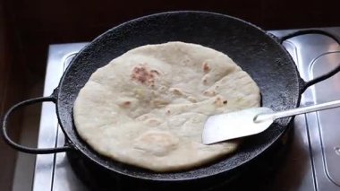 Demir bir Tawa 'da yassı ekmek ya da paratha pişirmek, lezzetli bir sabah kahvaltısı için mutfak sobasında çelik bir spatula ile nazikçe bastırıp çevirmek..