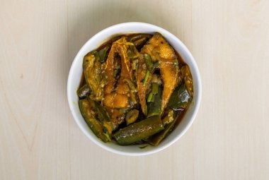 Hilsa balığıyla (Tenualosa ilisha) pişirilmiş lezzetli bir brinjal köri, açık ahşap bir yüzeyde beyaz bir kase içinde servis edilir. Üst görünüm.