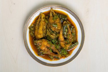 Popüler bir Bengali yemeği olan bu lezzetli brinjal köri Hilsa balığına (Tenualosa ilisha) sahiptir ve hafif ahşap bir yüzey üzerinde seramik bir tabakta sunulmaktadır. Üst görünüm.