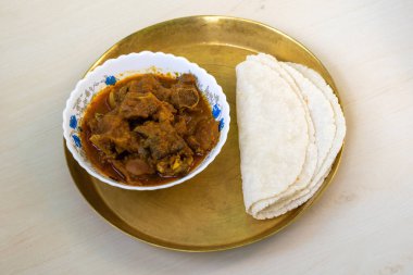 Hafif ahşap bir yüzeyde pirinç bir tabakta servis edilen lezzetli koyun eti ve roti (yassı ekmek). Çok lezzetli bir Bengali yemeği..
