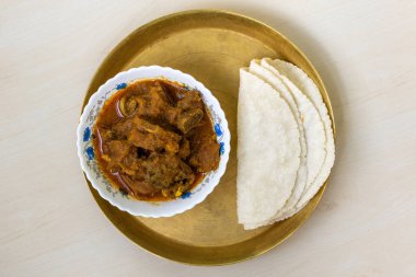 Hafif ahşap bir yüzeyde pirinç bir tabakta servis edilen lezzetli koyun eti körili ve roti yassı ekmeği çok lezzetli bir Bengali yemeği. Üst görünüm.