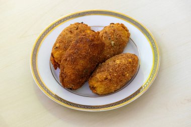 Beyaz bir tabakta, hafif ahşap bir yüzeye dayanmış ev yapımı, loş bir pirzola. Yumurta pirzolası ya da dimer alur pirzolası olarak da bilinen bu lezzetli yemek Bangladeş mutfağında çok popüler bir aperatiftir..