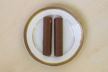 Çikolata kremalı iki çikolatalı bisküvi beyaz bir seramik tabakta tahta bir masanın üzerinde oturur. Tatlı arzularını tatmin etmek için mükemmel bir atıştırmalık. Üst görünüm.