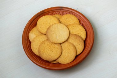 Tahta bir masada kil tabakta çıtır çıtır ve baharatlı bisküviler. Bu bisküvilerin tadı cips ve bisküvinin enfes bir birleşimi gibi. Öğleden sonra atıştırmalığı olarak ya da boş zamanlarında kullanılabilir..