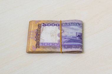 Bin tane Bangladeş Taka banknotundan oluşan küçük bir deste, hafif ahşap bir yüzeye lastik bantla bağlanmış. BDT 1000 Tk 'ye yakın çekim.