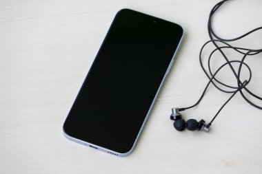 Bir akıllı telefon ve hafif ahşap bir yüzeye bağlı siyah kulaklık..