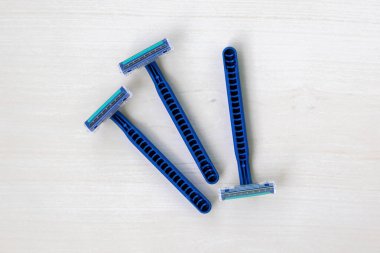 Açık ahşap zemin üzerinde keskin bıçakları olan üç yeni mavi tıraş bıçağı. Üst görünüm.