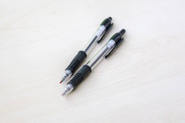 İki tükenmez kalem, hem çalışmak hem de çalışmak için temel araçlar olan hafif ahşap bir yüzeyde dinleniyor..