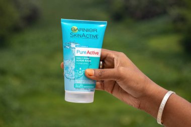 Garnier Cilt Aktif Günlük Pore yüz temizleme tüpü ve yeşil doğa özgeçmişi olan kadın eli. Yüz temizleyici kiri temizliyor..