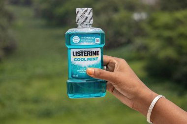 Listerine Cool Mint 250 ml gargara kadın elinde, yeşil doğa arka planı. Günlük ağız temizliği, taze nefes ve sağlıklı diş etleri için gereklidir..