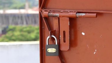 Yanmış turuncu boyalı metal bir kapının kilidine yakın çekim, bir evin çatısından çekilmiş..