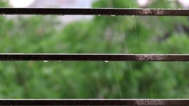 Yağmur damlaları paslanmaz çelik bir balkon çitine düşer ve su sıçratır. Rahatlatıcı bir doğal etki yaratır. Çelik boruya yakın çekim su damlaları.