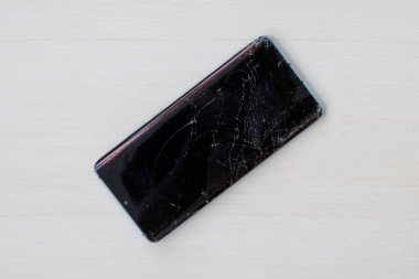 Ahşap arka planda çatlak ekranlı akıllı telefon. Hasarlı cep telefonu görüntüsünün üst görüntüsü. Tamir edilmesi gereken kırık bir cep telefonu..