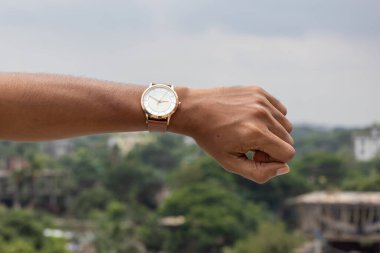 Deri kayışlı analog saati olan bir adamın eli zamanı kontrol ediyor. Doğanın bokeh arka planı. Zaman yönetimi ve dakiklik kavramı.